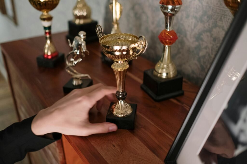 pexels-photo-6565255-6565255 A close-up of a hand reaching for a shiny trophy on a wooden shelf, symbolizing success.